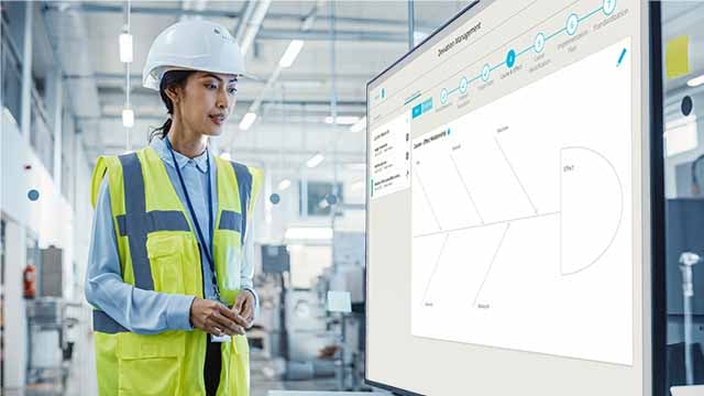 Frau mit Schutzhelm betrachtet Ishikawa-Diagramm auf digitalem Shopfloor Board